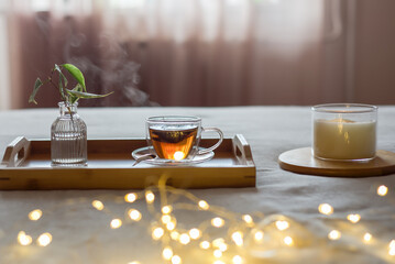 Hot tea in transparent cup on tray in bedroom in winter or autumn. Hygge concept