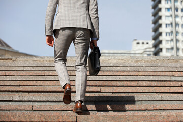 Man in a business suit with leather briefcase climbing stone stairs in city, male legs in motion on...