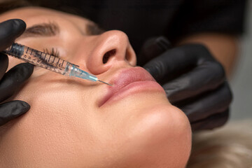 Woman getting cosmetic injection of botulinum to lips. Lip augmentation procedure in a beauty salon. Focus on lips