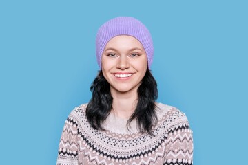 Portrait of young woman in hat in sweater on blue background