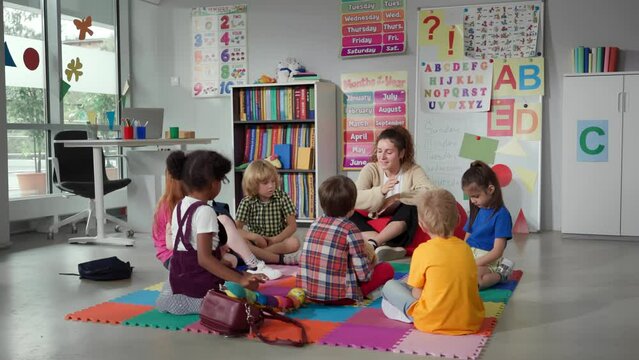 Small nursery school children with teacher sitting on floor having lesson