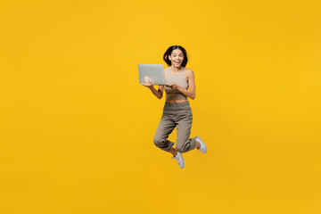 Full body overjoyed young latin woman 30s she wear basic beige tank shirt hold use work on laptop...