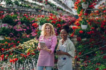 Multiracial female florists working in a green house plant nursery and using tablet