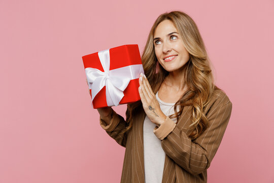 Young Wistful Dreamful Successful Employee Business Woman 30s She Wear Casual Classic Jacket Hold Red Present Box With Gift Ribbon Bow Isolated On Plain Pastel Light Pink Background Studio Portrait.