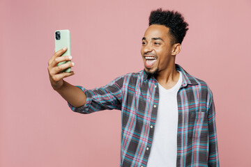 Young smiling happy man of African American ethnicity he wear blue shirt doing selfie shot on mobile cell phone isolated on plain pastel light pink background studio portrait People lifestyle concept