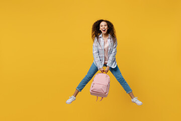 Full body young smiling happy black teen girl student she wear casual clothes hold backpack bag jump high look camera isolated on plain yellow color background. High school university college concept.