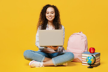 Full body fun young black teen girl student she wear casual clothes backpack bag hold use work on laptop pc computer isolated on plain yellow color background. High school university college concept.