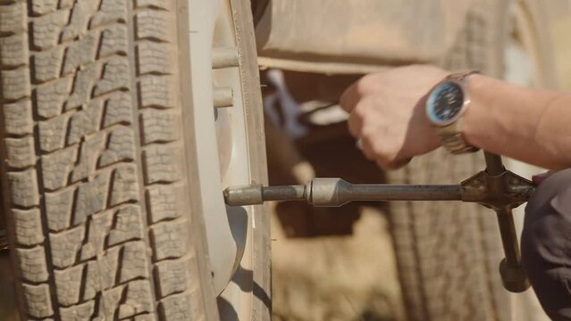 Man removes nuts from the wheel with a transverse wrench, side view. Replacing a wheel on an off-road car. Preparing the car for arrival