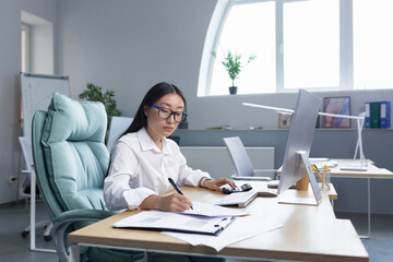 Work with documents. Portrait of a young beautiful business woman Asian accountant works with documents and reports. Sitting at the desk in the office, writing.