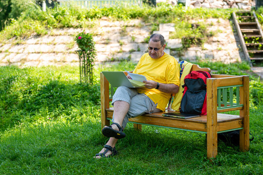 Middle Aged Man With Laptop And Documents Working Outside In Garden, Green Home Office Concept.