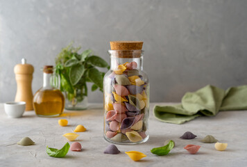 Multi-coloured Italian pasta conchiglie or seashells in glass bottle, olive oil, olive branch. Concrete background 