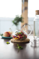 A glass teapot with fruits and berries, mint leaves, a bottle of water on the table outside. Summer fruit tea.