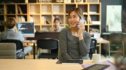 Confident female manager having phone conversation while sitting in a software develop company office