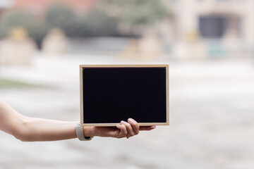 Female hand holding empty blank board with copy space outdoor. Template for design, special offer and advertising