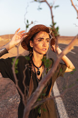 Portrait of a beautiful girl in a hat on the background of a road in the desert. In the foreground is a tree branch.