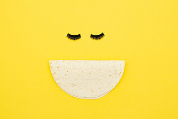 Smiley face made of fake eyelashes and tortilla. National taco day concept. 