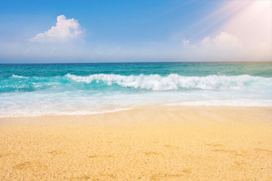 Beautiful expressive background image of golden mediterranean sandy beach, sea surf with a white foam, turquoise water and blue sky with white clouds on bright summer sunny day.