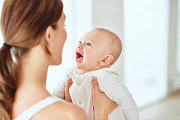 Mother playing and bonding with cute baby boy and having fun indoors at home together. Loving mom holding her beautiful, playful and free child in the air. Woman enjoying spending time with her kid