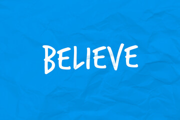Testo Believe, scritto su carta stropicciata stile post it di colore blu. Messaggio positivo.