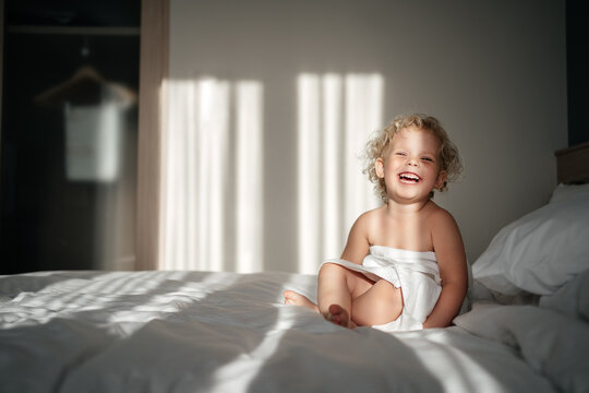 child in a hotel with a smile and an emotion of happiness sits on a bed in a towel with morning rays of light. Vacation