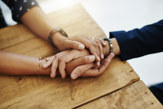 Hands holding abuse victim in a therapy session for support and comfort by a professional psychologist on a wooden table. Kind and caring therapist touching to show care and affection in counseling