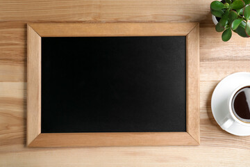 Clean small chalkboard, coffee and plant on wooden table, flat lay