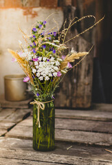 A cute bouquet of colorful wildflowers in a glass vase stands on old boards. still life in a cozy rustic style, life in the village