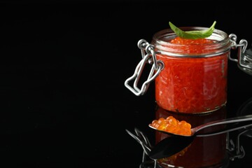 Delicious red caviar and basil leaf on black background. Space for text