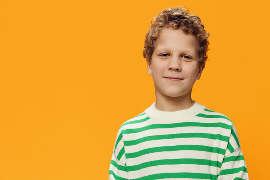 horizontal portrait of a cute curly boy of school age in a striped long-sleeved t-shirt on an orange background