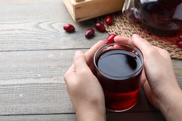 Woman with cup of fresh dogwood tea at wooden table, closeup. Space for text