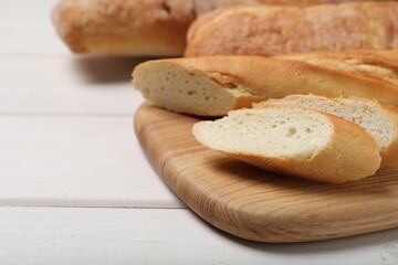 Cut tasty baguette on white wooden table, closeup. Space for text