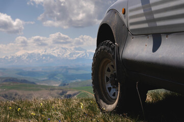 Fototapeta na wymiar SUV wheel on the off-road adventure trail against the backdrop of mountains in the clouds
