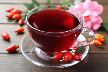 Aromatic rose hip tea and fresh berries on wooden table, closeup