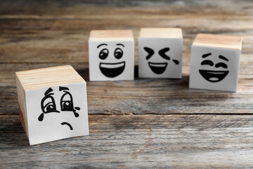 Cubes with sad and funny faces on wooden table. Bullying concept