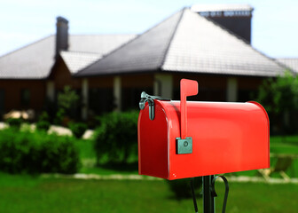Red letter box and blurred view of modern house with beautiful garden on sunny day
