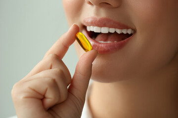 Young woman taking dietary supplement pill on blurred background, closeup - obrazy, fototapety, plakaty