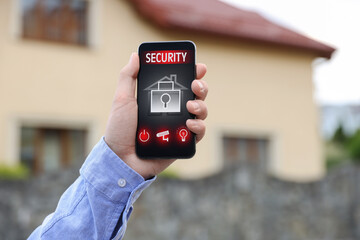 Man using home security application on smartphone in front of house outdoors, closeup