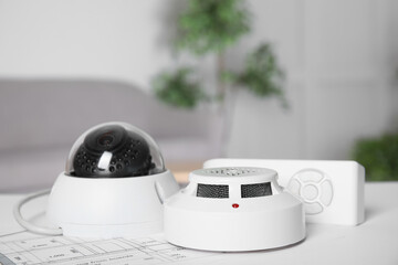 CCTV camera, remote control, smoke detector and building plan on table indoors. Home security system