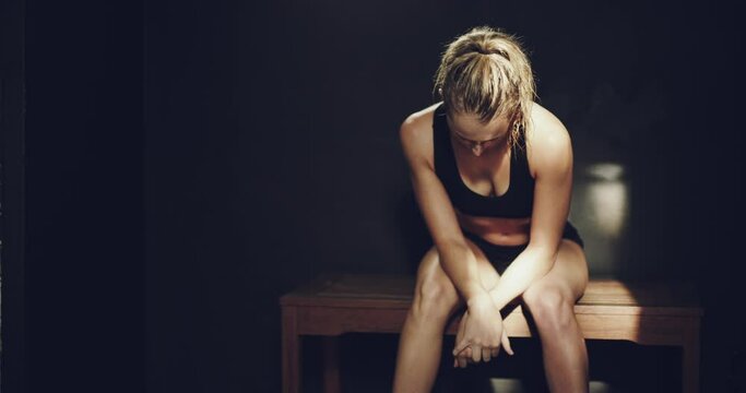 Fit, healthy and tired woman sitting in the changing room after a long athletic workout routine and exercise session in the gym or fitness centre. Active female athlete taking a break after training.