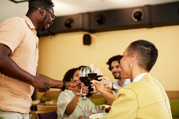 Interracial friends are raising wine glasses and celebrating a happy event in a restaurant.