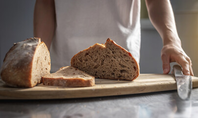 Baker cuts freshly baked bread with a knife to check the quality. Production of bakery products as...