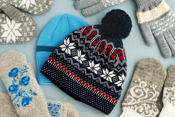 Clothing for autumn and winter in the form of hats, mittens and gloves. Hats, mittens and gloves on a blue background. Knitted clothes for cold seasons.