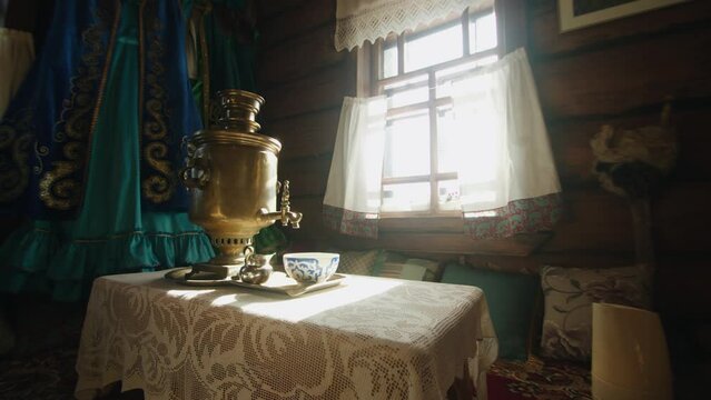 Cozy interior of a rustic wooden house with a samovar on a table in bright sunlight from a window with white curtains