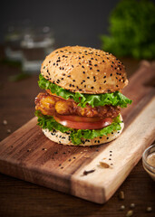 Homemade chicken burger with tomato and special sauce served on paper on a wooden cutting board.Selective focus.