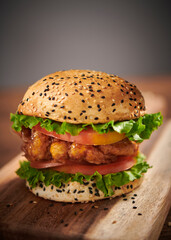 Fresh chicken burger with special sauce on wooden cutting board. Selective focus.