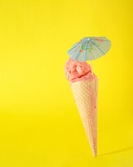 Ice cream cone on a vibrant yellow background with cocktail umbrella. Peachy, pink ice cream balls...