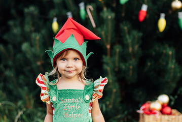 Fototapeta Child waiting for Christmas in wood in juli. portrait of little girl near christmas tree. Baby decorating pine. winter holidays and people concept. Merry Christmas and Happy Holidays. obraz