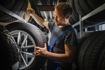 Fototapeta Hardworking experienced worker holding tire and he wants to change it In the tire store. Selective focus on tire. obraz