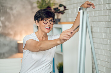 Mature dark-haired woman standing near the flipchart and working on project details