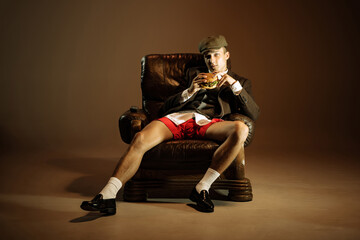 Young man, retro 1920s style english gangster jacket, shorts and cap tasting fast food isolated...